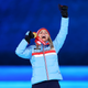 Gold medallist Therese Johaug, wearing a blue jacket with a red stripe and black gloves, holds her gold medal with one hand, has her other fist in the air, and is cheering victoriously at the Women's 30km Mass Start medal ceremony during the Beijing 2022 Winter Olympics Closing Ceremony on Day 16 of the Beijing 2022 Winter Olympics.